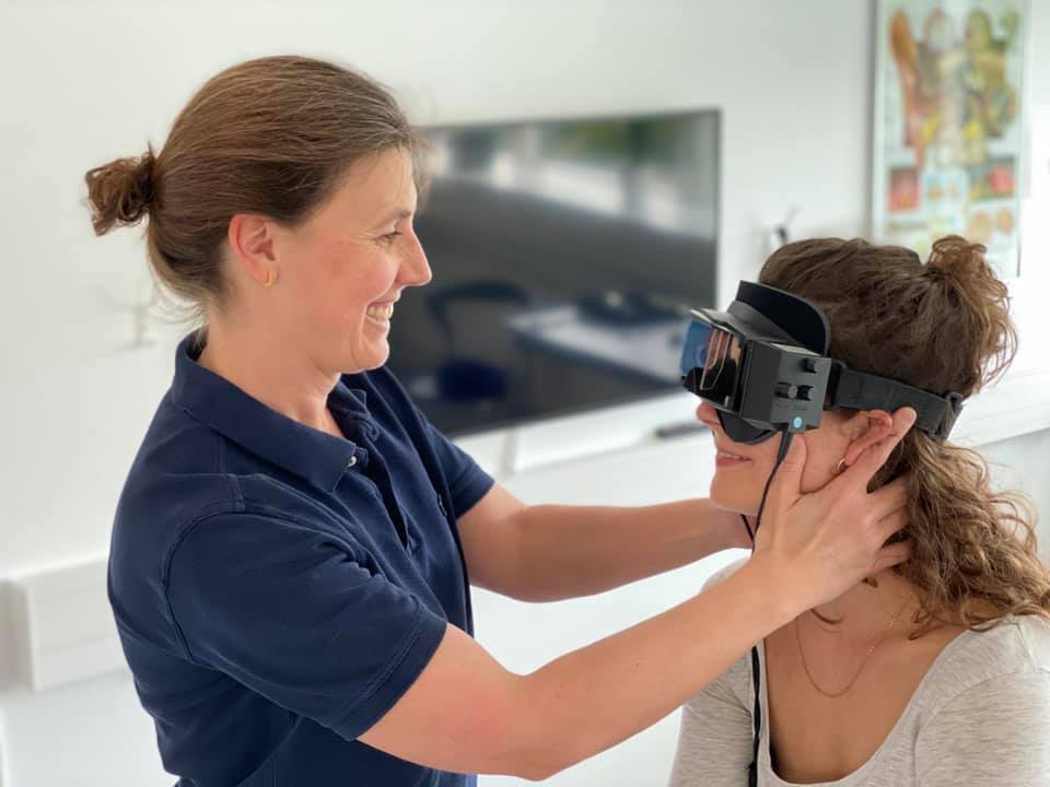 Kvinna som monterar VR-headset på en annan person, leende. Inomhus, undersökande.
