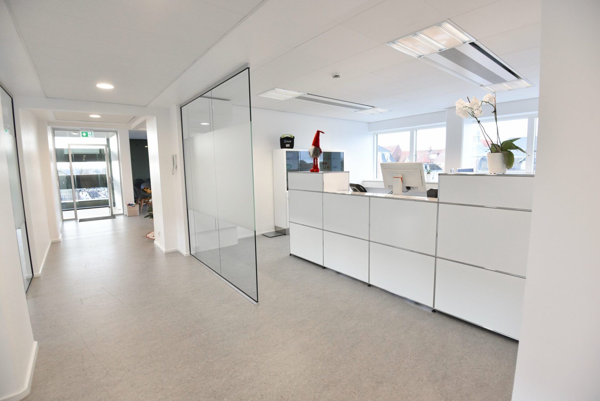 Ljus kontorsinredning med vit receptionsdisk, glaspartition och hall.