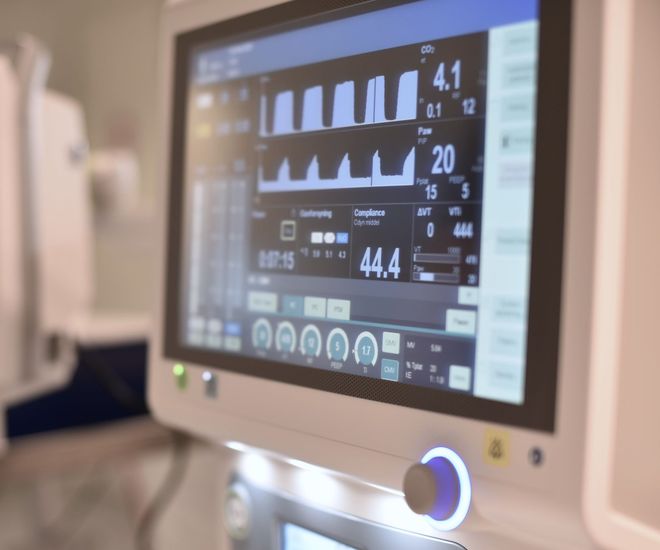 Medicinsk monitor som visar vitala tecken och vågformer i en sjukhusmiljö.