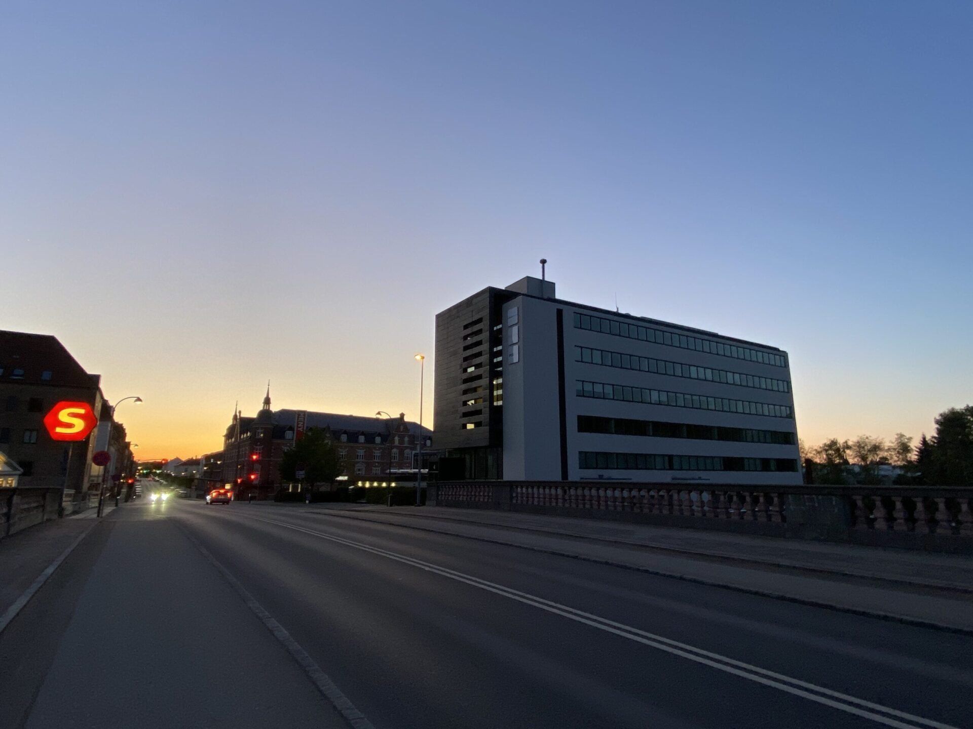 Väg med byggnader, inklusive ett stort hotell, i skymningen. Orange och blå himmel.