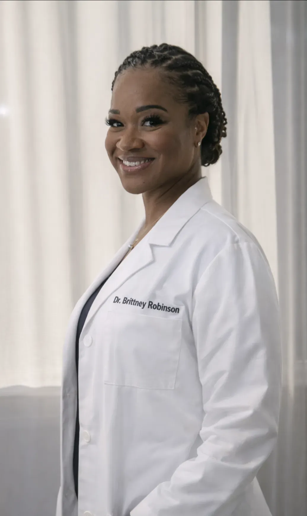 A woman in a white lab coat is sitting at a desk in front of a mirror.