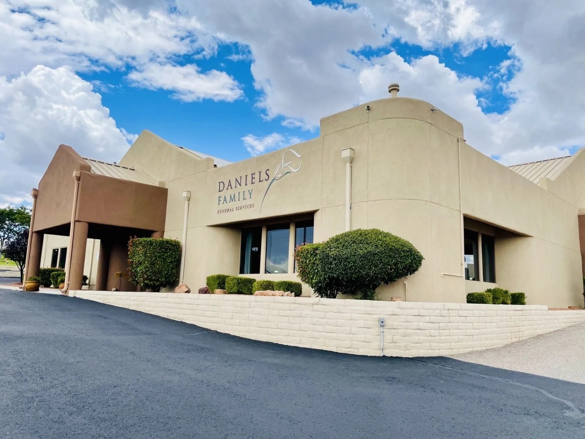 Beige stucco building with bell tower, arched windows, red tile roof, and blue sky.