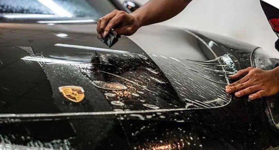 A person is applying a protective film to the hood of a car.