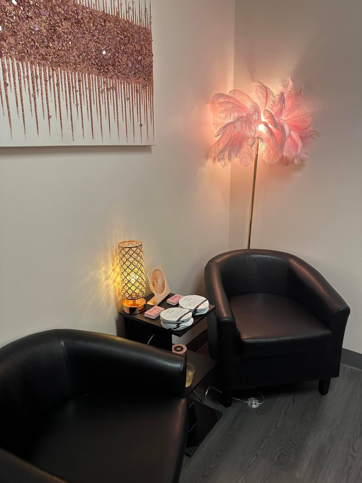 Two black armchairs and a table with lamp in a corner lit with soft pink light.