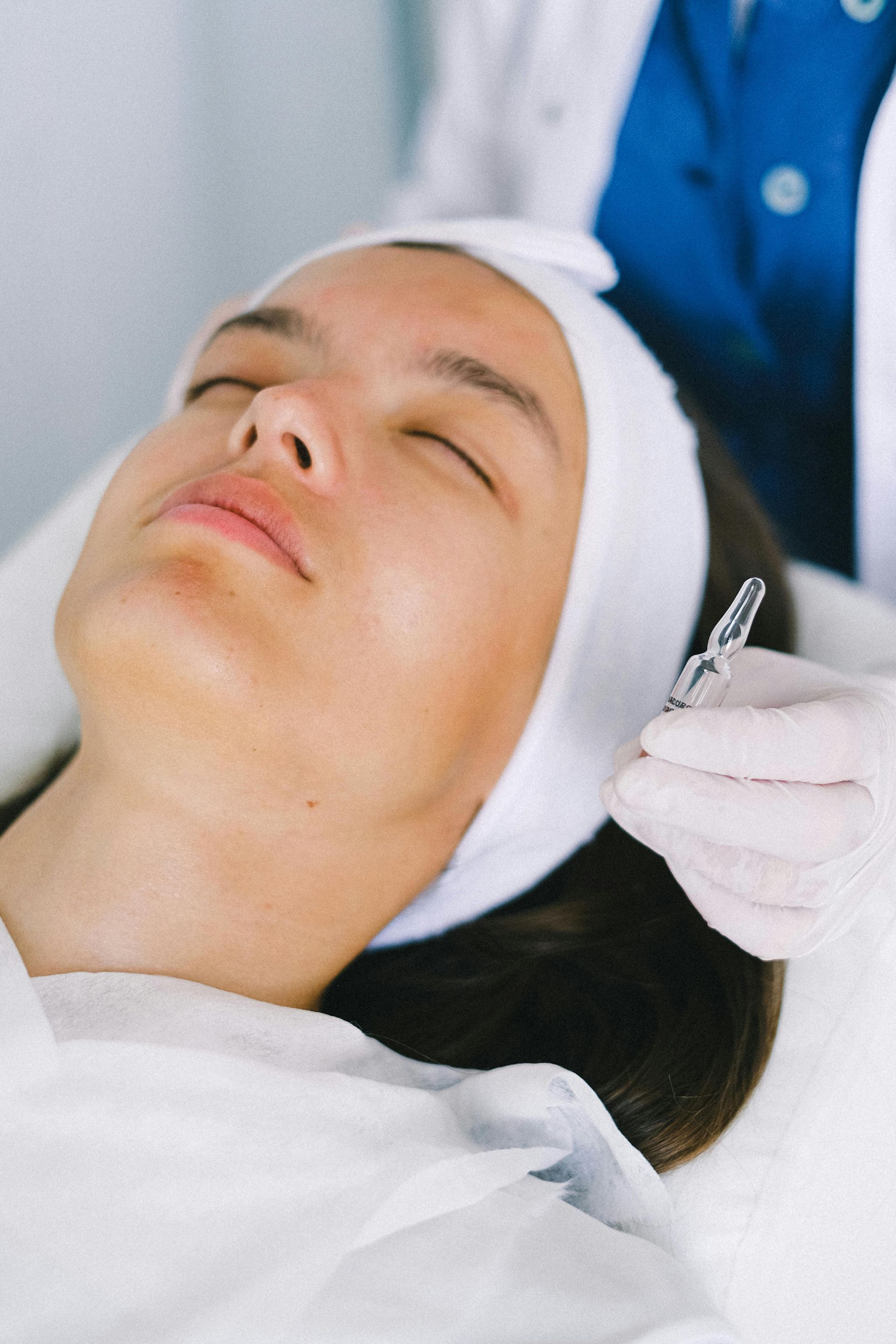Woman receiving a facial treatment, eyes closed, with medical professional holding a vial.