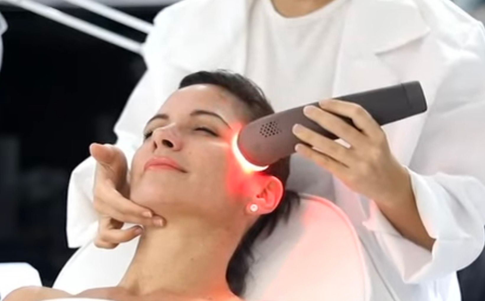 Woman receiving red light therapy treatment on her face, in a medical setting.