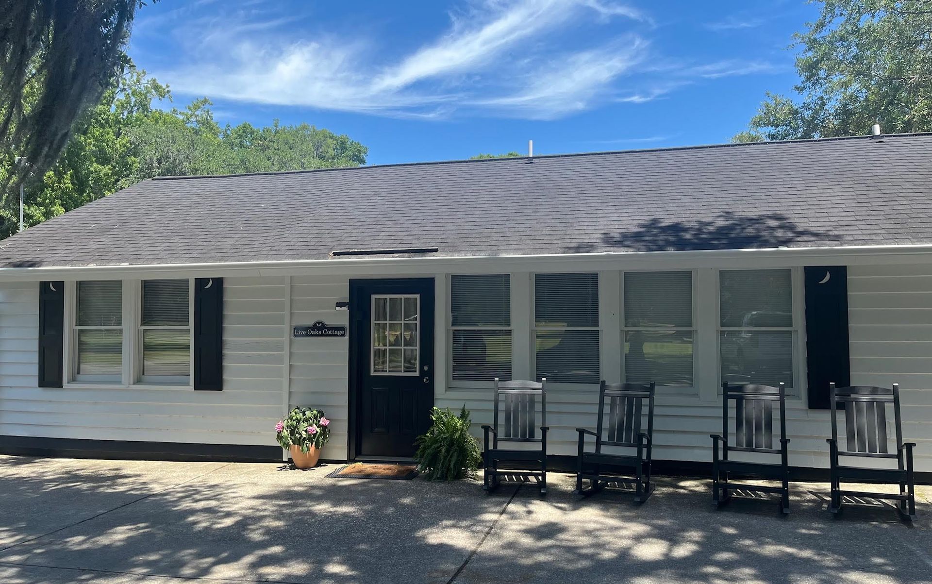 A white house with black shutters and rocking chairs in front of it.