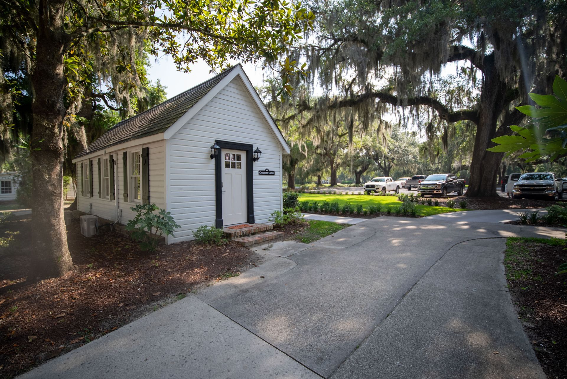 a small white house with a black door is surrounded by trees and a driveway .