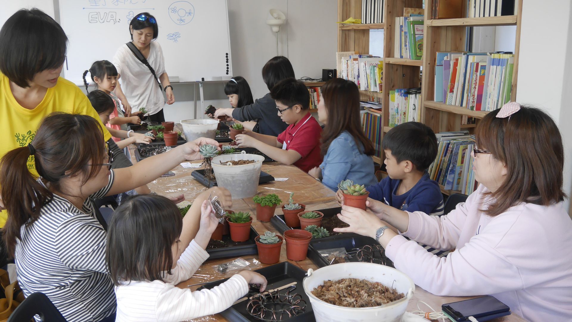 一群人圍坐在桌旁，在室內團體園藝活動中將植物種進盆栽裡