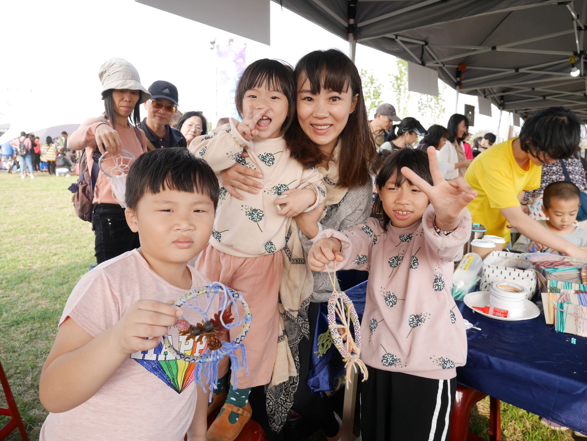 孩子們在有遮蔭的戶外活動中，開心地微笑並拿著手工作品