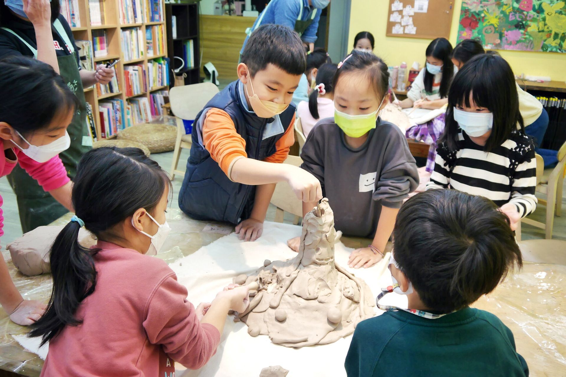 戴著口罩的孩子們在教室裡圍著桌子一起捏黏土。