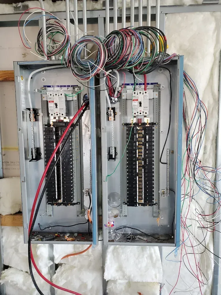 Two electrical panels with exposed wiring against an insulated wall.