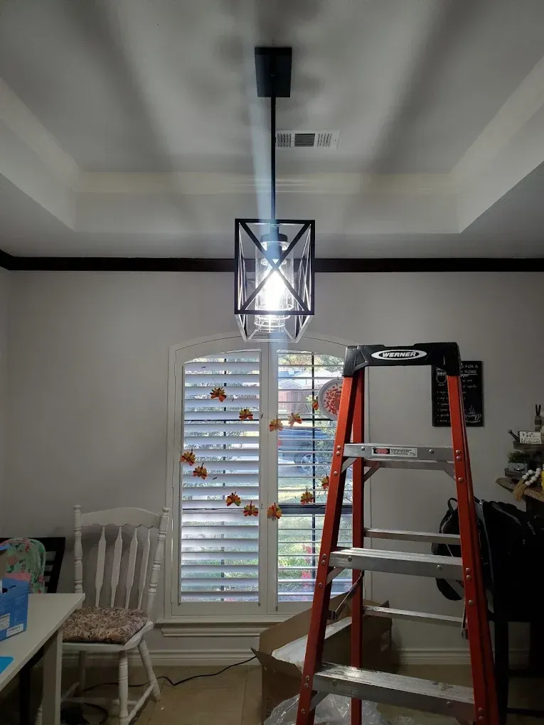 A black pendant light fixture hangs from a white ceiling. A stepladder stands below.