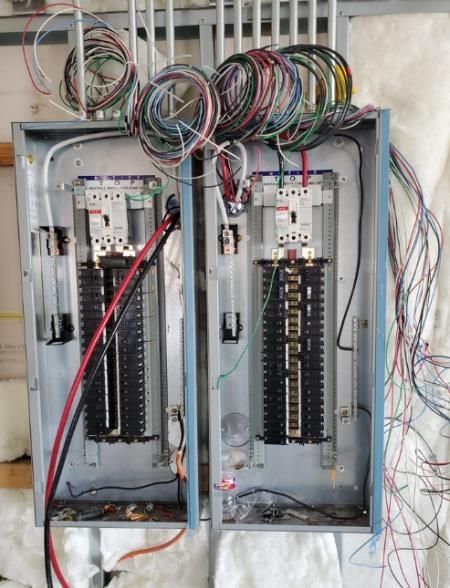 Open electrical panel with numerous colored wires spilling out, unfinished installation.