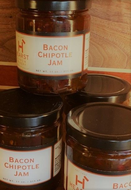 Three jars of bacon chipotle jam on a wooden surface