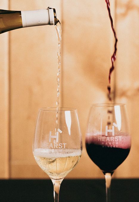 Wine being poured into two glasses, one white and one red, on a warm-toned background