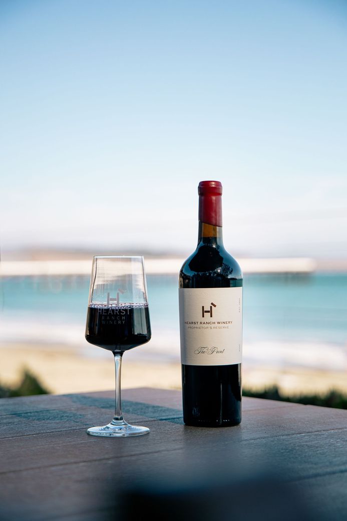 Hand placing a wine bottle into a black Hearst Ranch shopping bag on a table outdoors