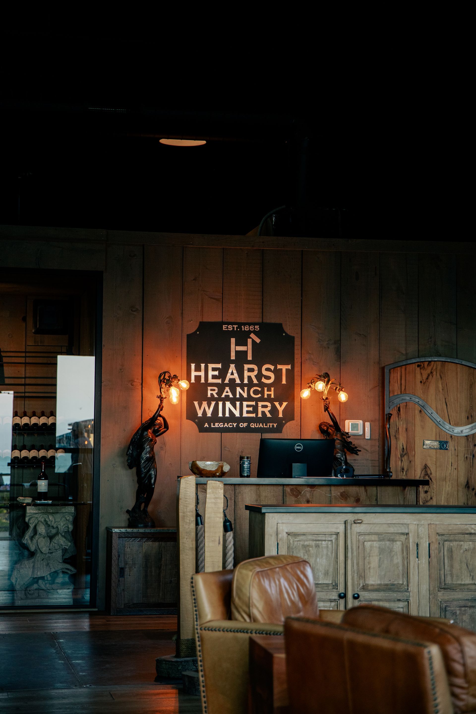 Three Hearst Ranch wine bottles on tan cardboard with a hand holding a black bottle above them
