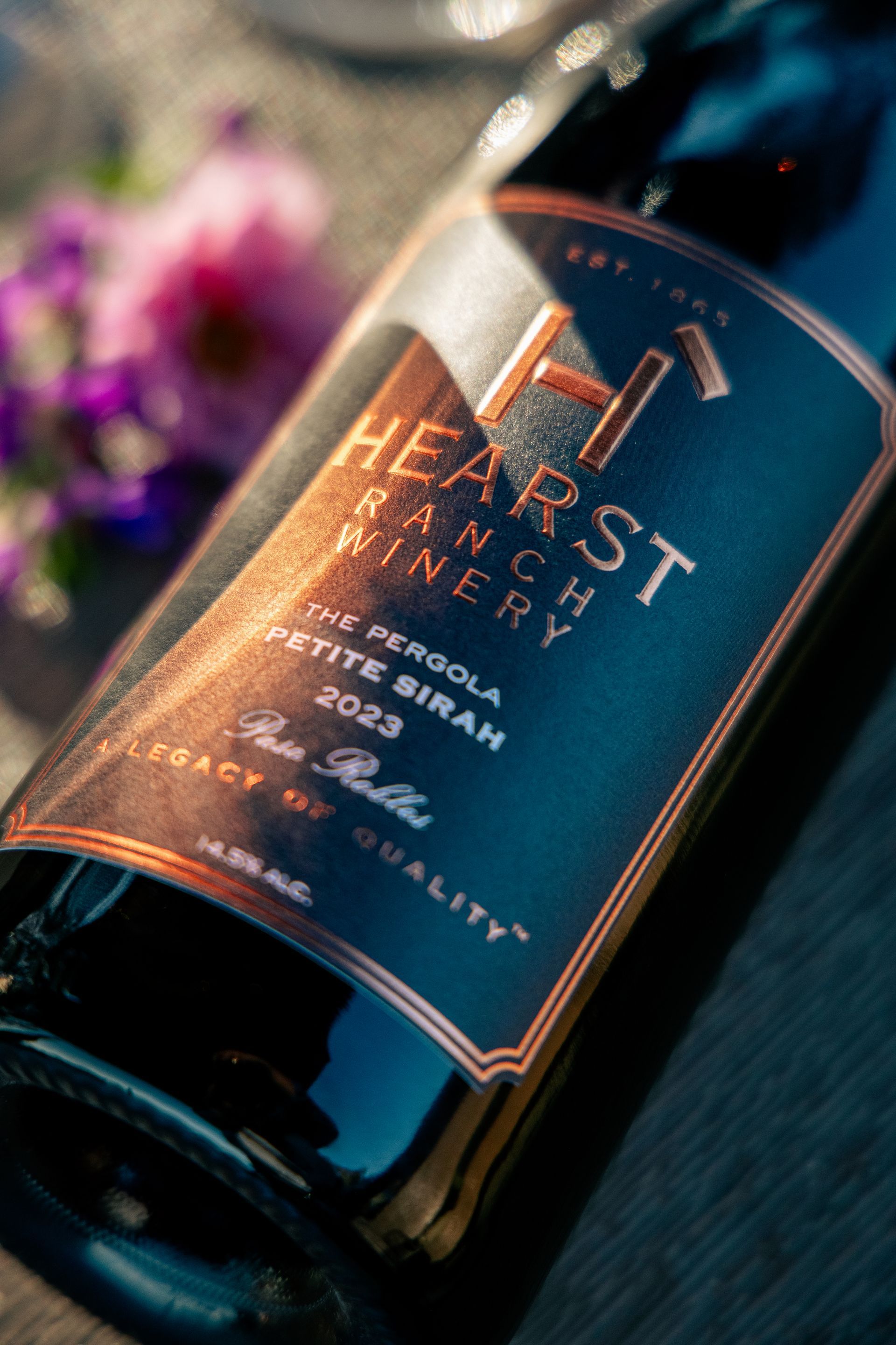 Wine glass and bottle on a table, with a hand holding the glass in a softly blurred outdoor setting