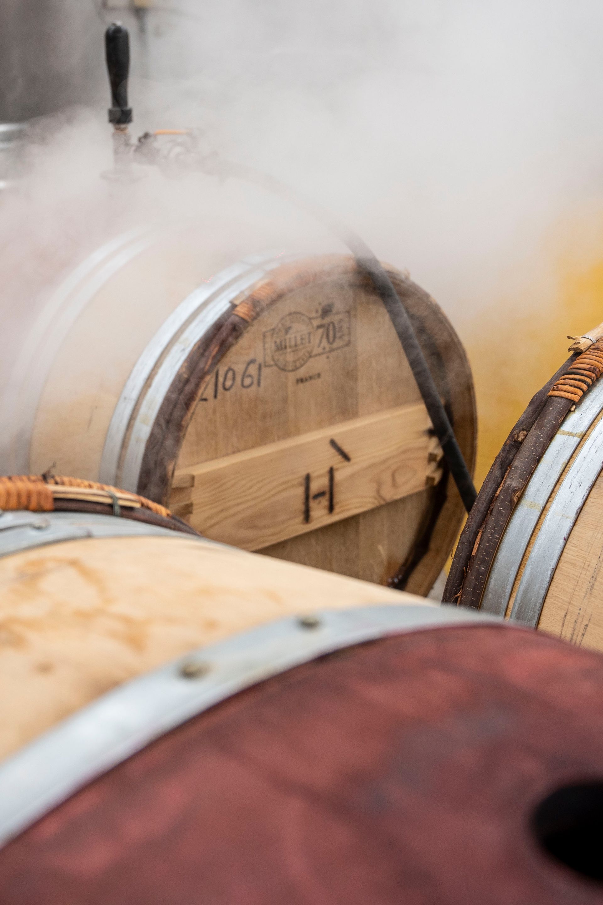 Wooden whiskey barrels aging in a misty cellar, with steam or vapor drifting around them