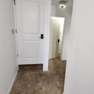 A view of a carpeted hallway with a closed white door in the foreground and a second white door further down the hall.