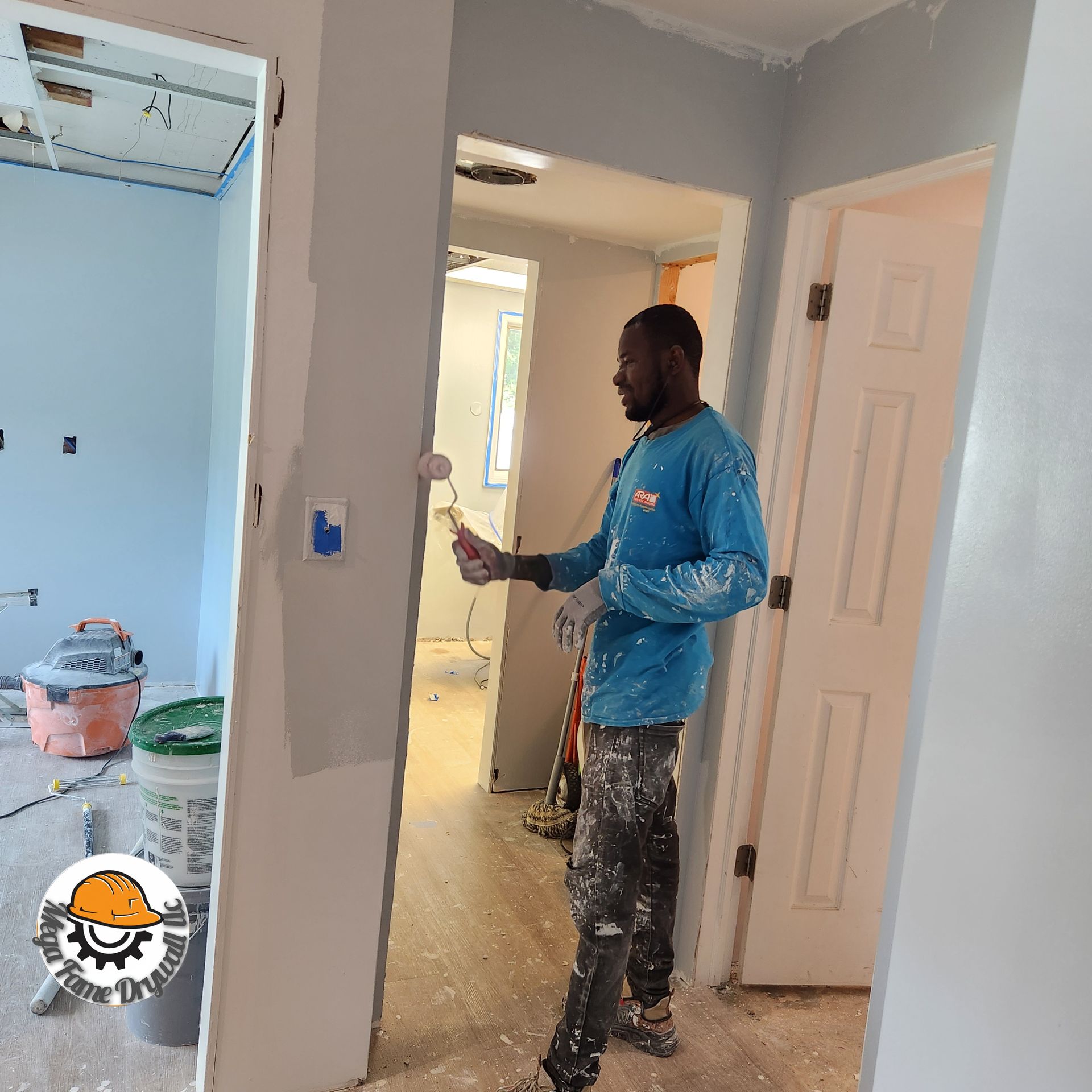 An empty room under renovation with light wood floors, gray walls, and large drywall sheets leaning against the wall.