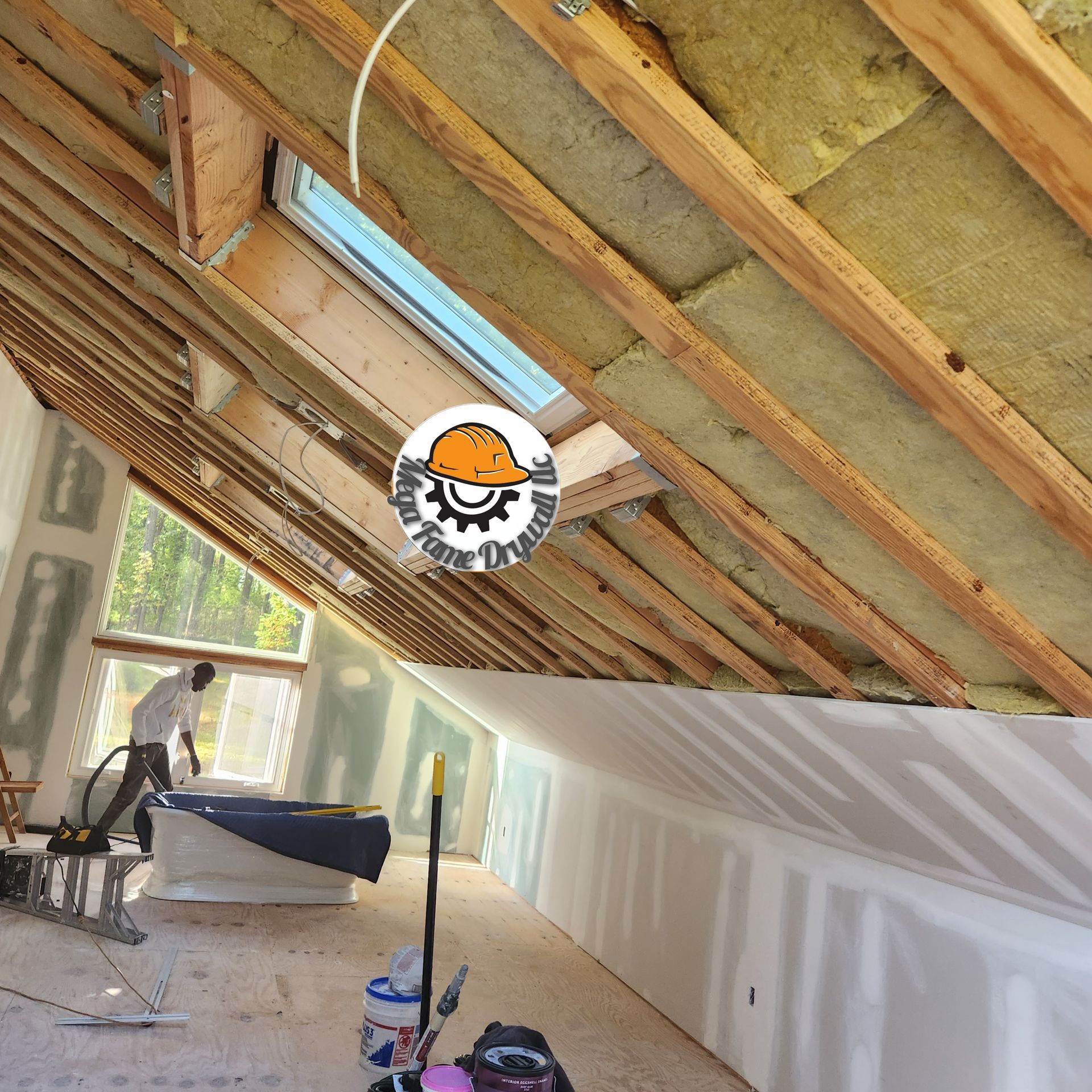 Sloped attic ceiling under renovation with exposed insulation, wood beams, drywall, and painting supplies below