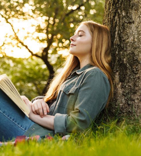 A woman is sitting under a tree reading a book