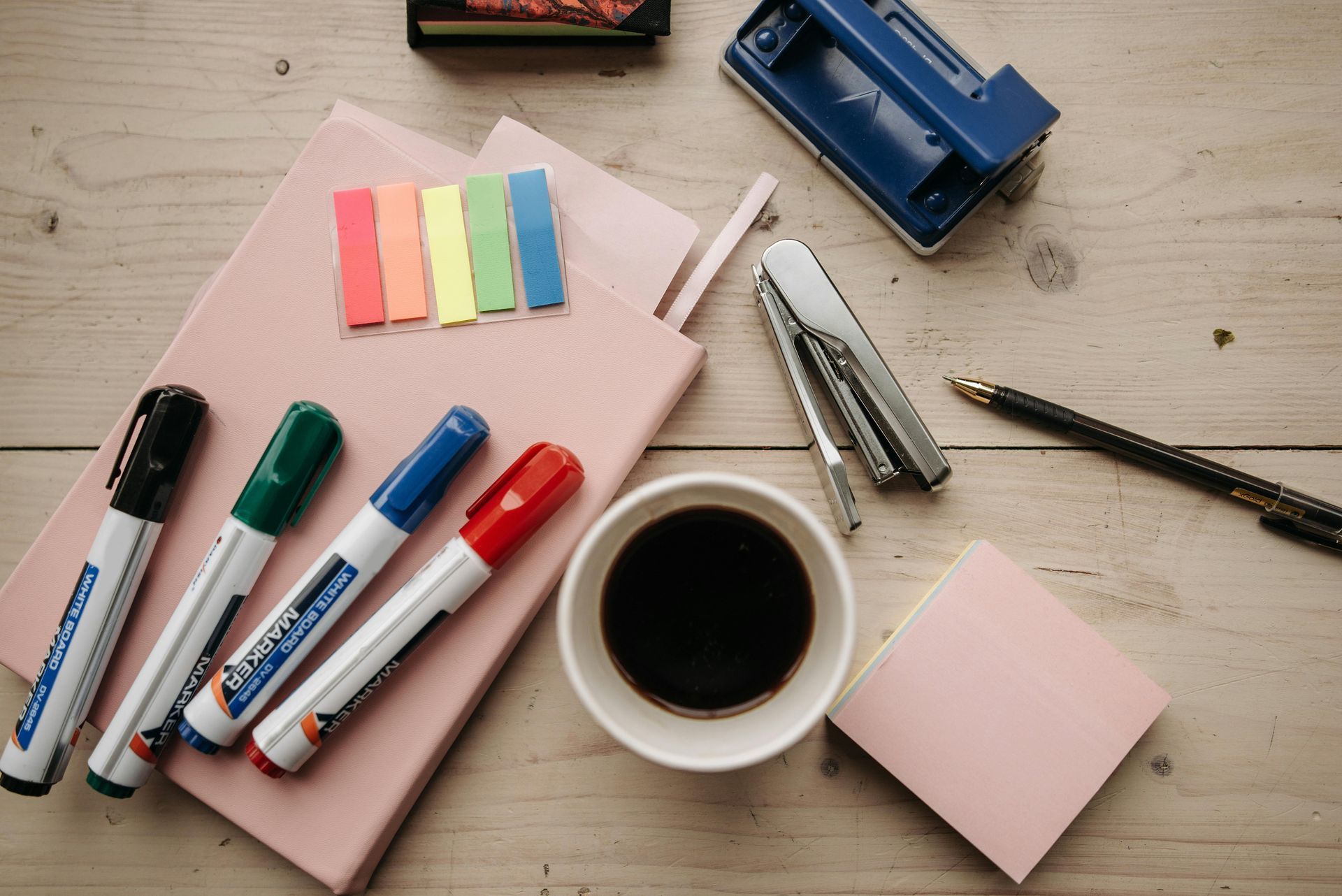 Schreibtisch mit Stiften, Notizbuch, Locher und Kaffeetasse in Arbeitsumgebung