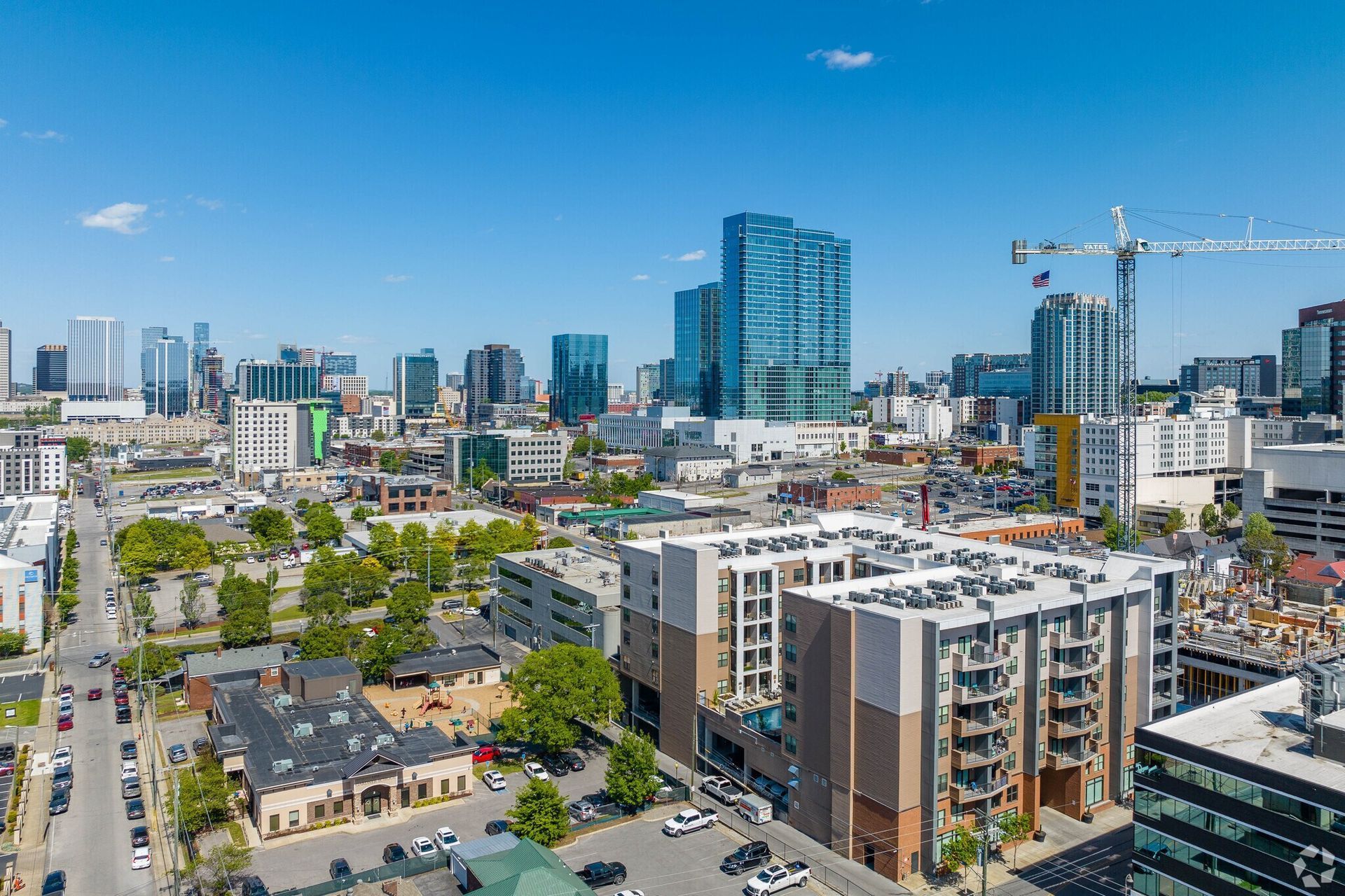 Aerial cityscape featuring modern apartment buildings and a construction crane against a clear blue sky.