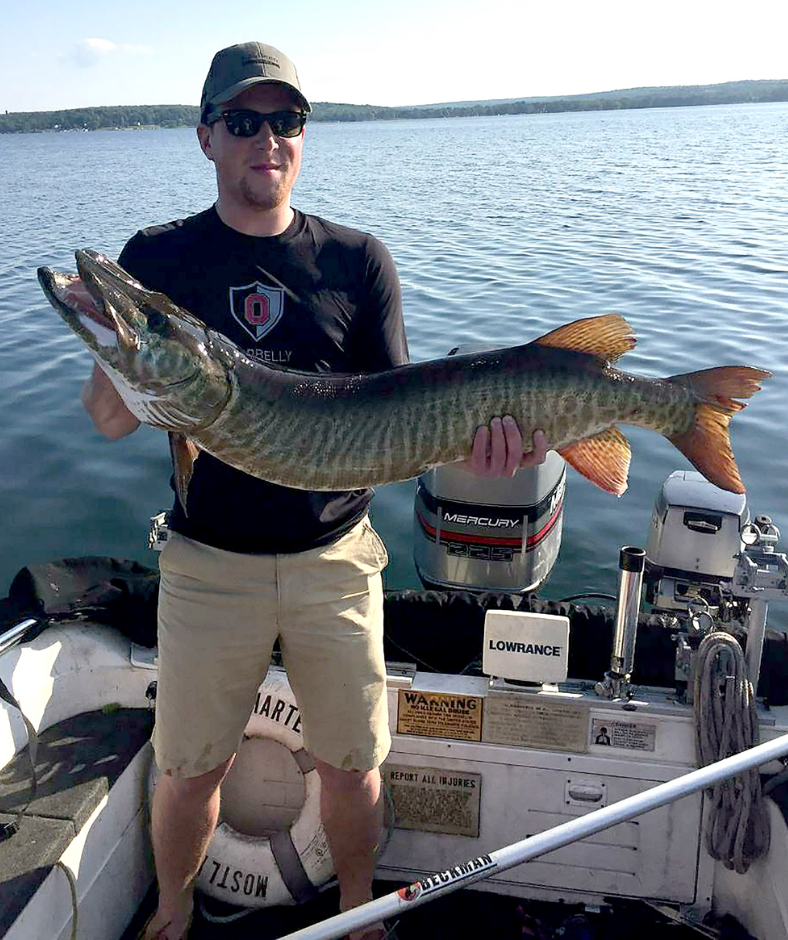 A man is standing on a boat holding a large fish.