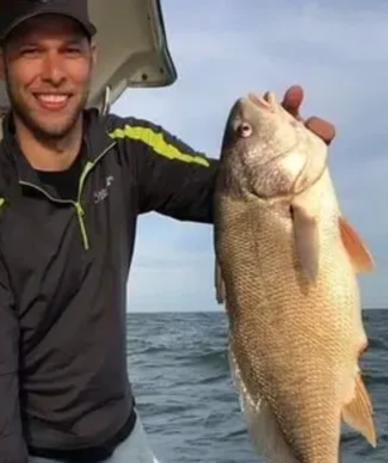 A man is holding a large fish in his hands on a boat.
