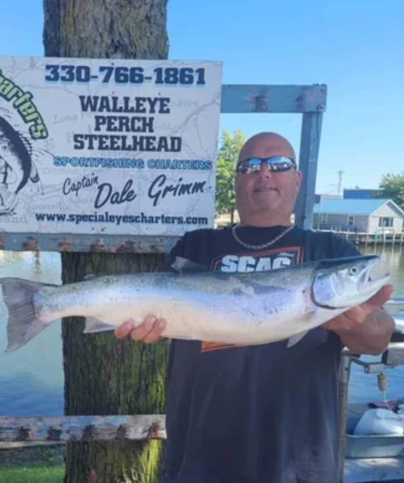 A man is holding a large fish in front of a sign that says walleye perch steelhead