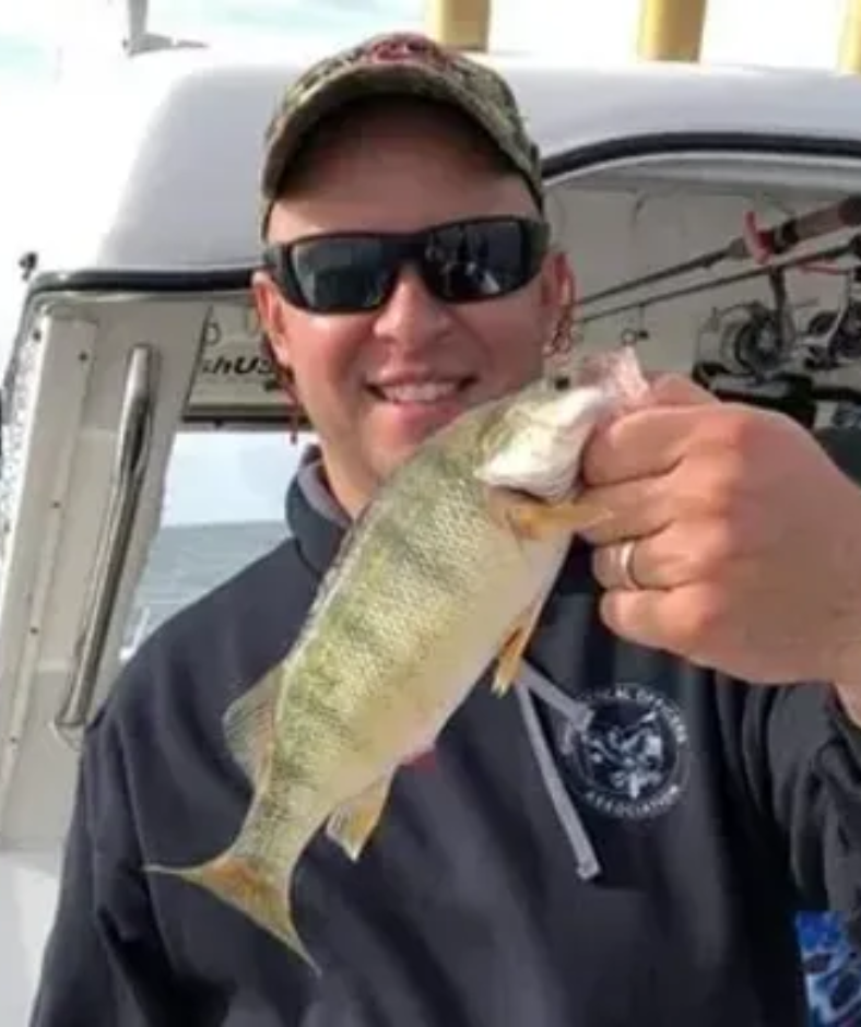 A man wearing sunglasses is holding a fish in his hand.