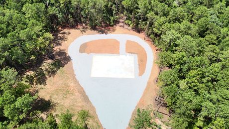 Aerial view of a cleared area in a forest, possibly for a house, with a gravel driveway and a white rectangle.