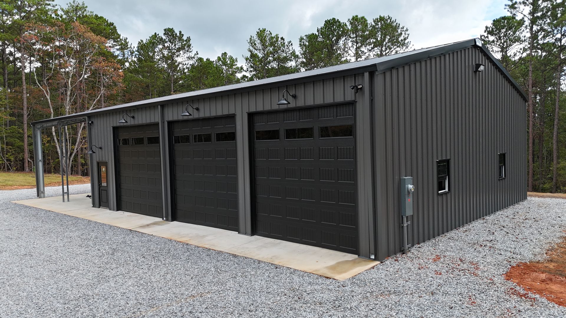 Three-bay dark gray metal garage with black doors on a gravel driveway.