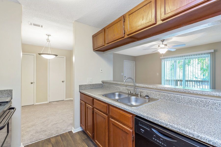 A kitchen with wood cabinets, granite-look countertops, and a double sink, opening to a living area with a sliding door.