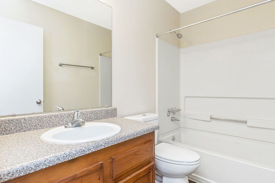 A bathroom featuring a light wood vanity, white sink, large mirror, and a white shower-tub combo against neutral walls.