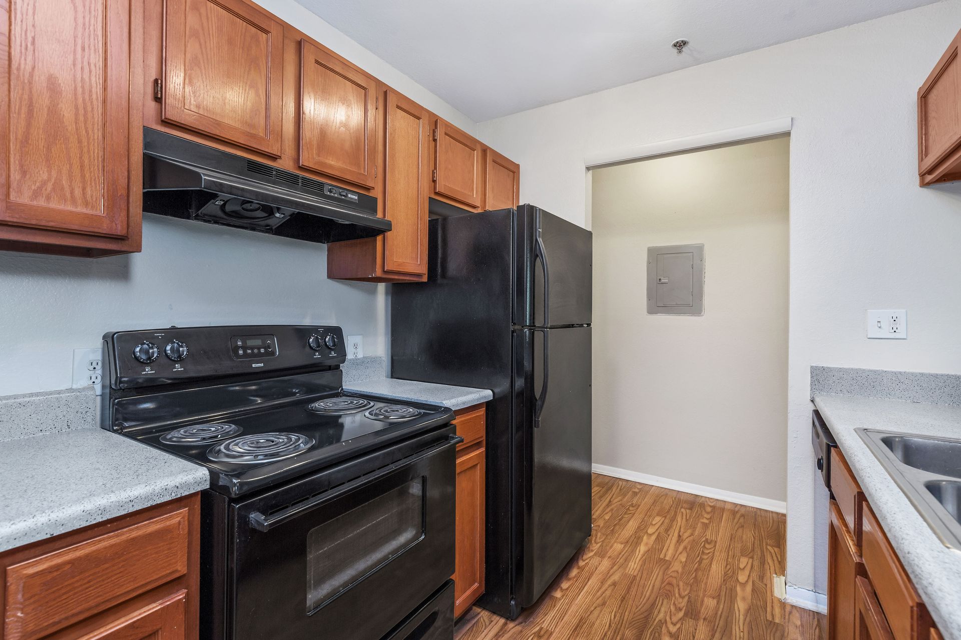 A kitchen with wood cabinets, granite-look countertops, and a double sink, opening to a living area with a sliding door.