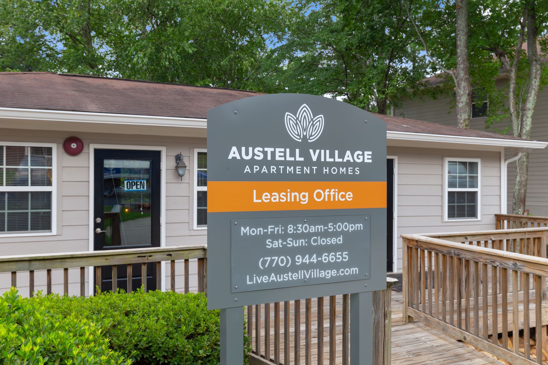 Sign for Austell Village Apartment Homes leasing office in front of a light-colored building with a wooden ramp.