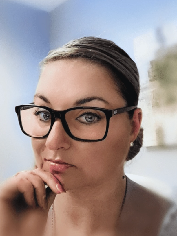 Woman with black glasses resting her chin on her hand, looking thoughtfully at the camera.