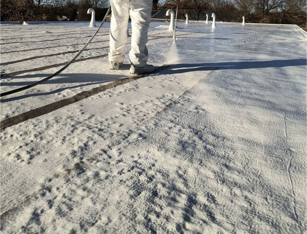 Worker in white coveralls spraying a frosty coating over a rooftop surface