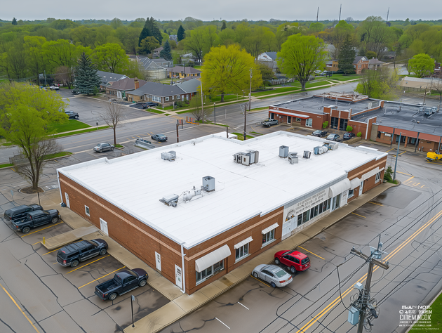 Aerial view of a snow-covered brick building with parked cars and trees nearby.