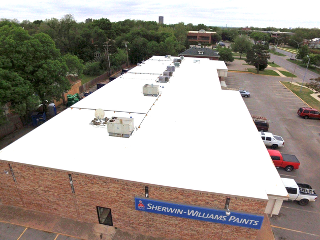 Aerial view of a brick building with a white roof and a Sherwin-Williams Paints sign, surrounded by trees and cars.