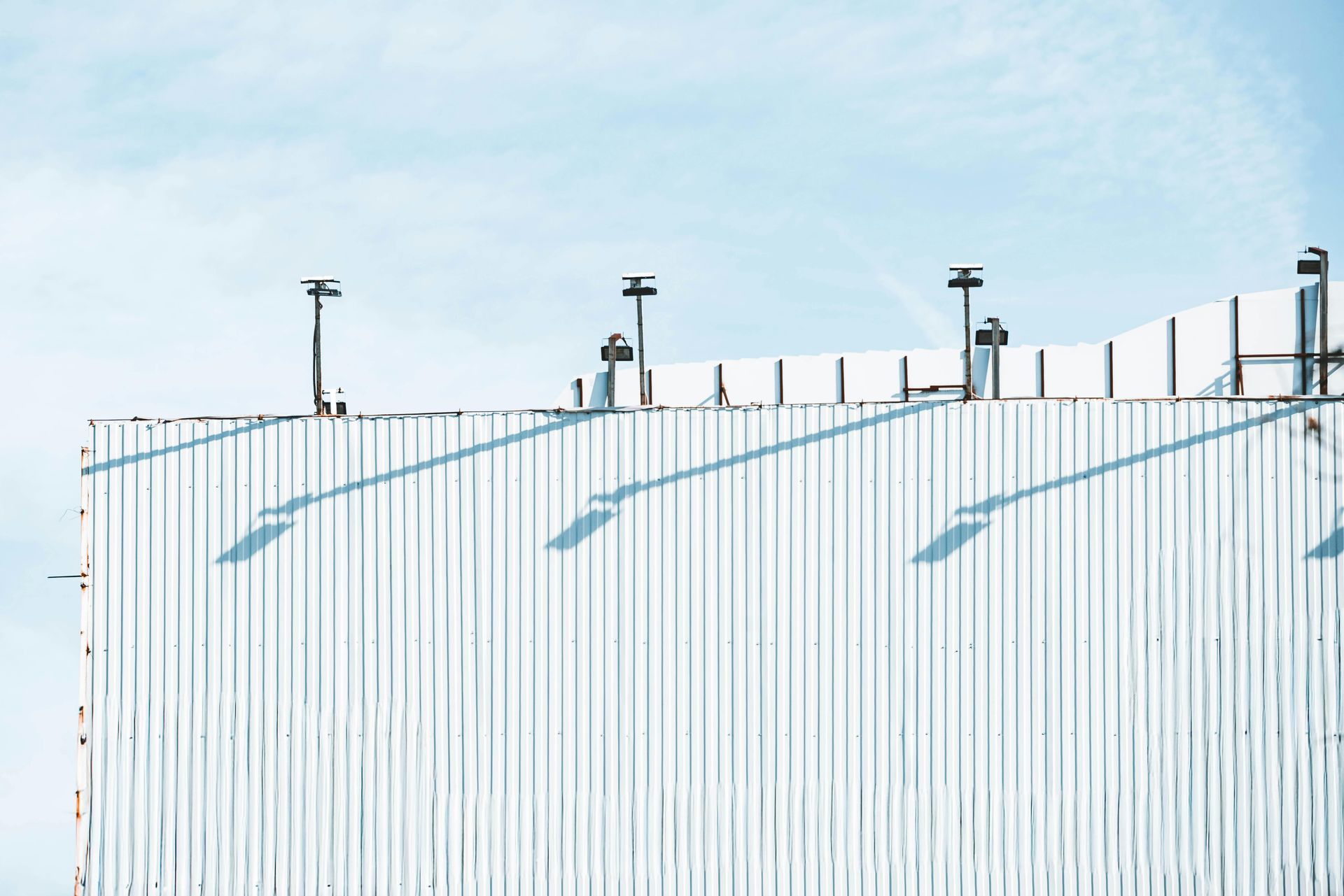 White metal fence with blue diagonal shadows under a pale sky