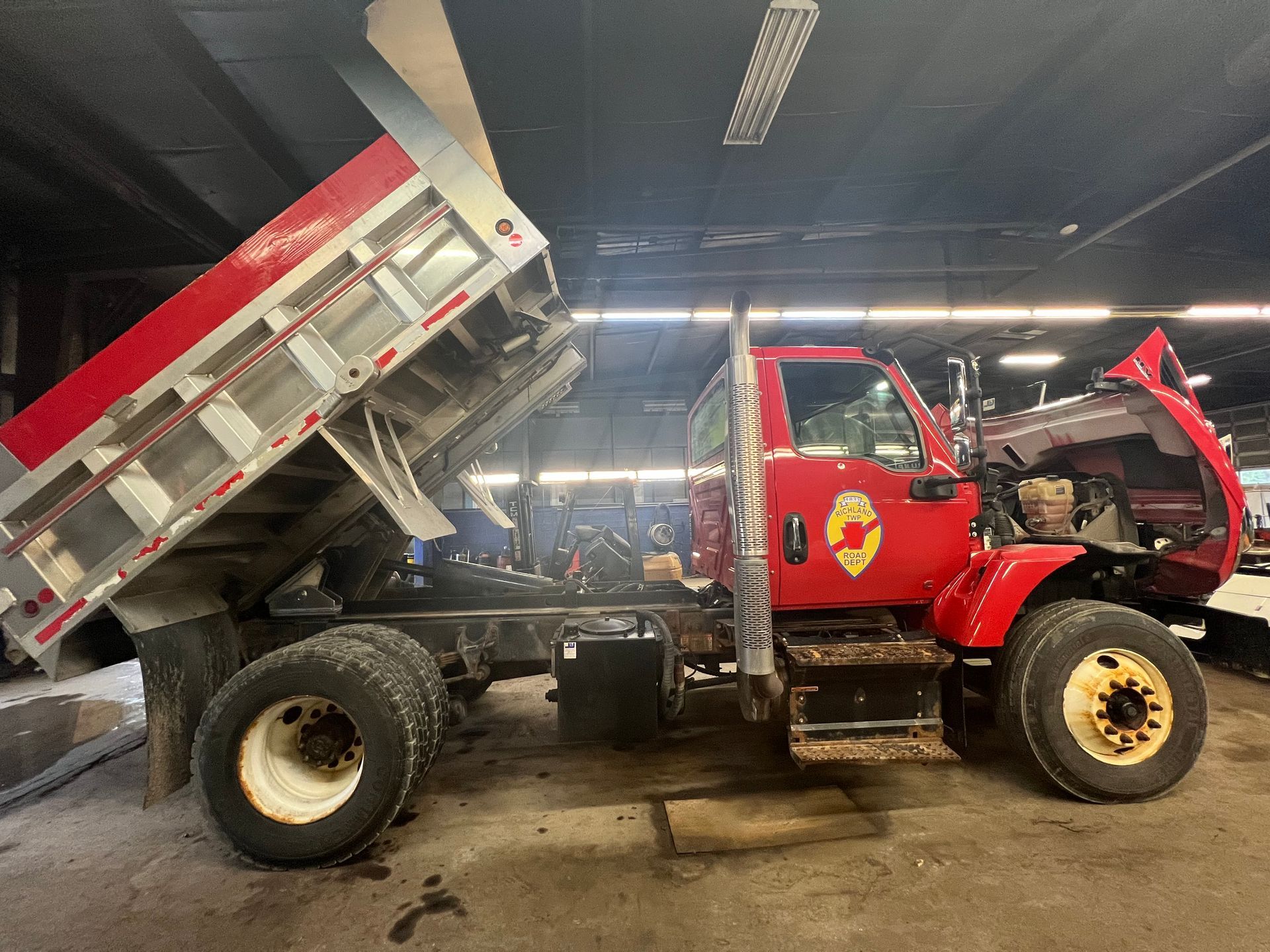 A red dump truck is being worked on in a garage.