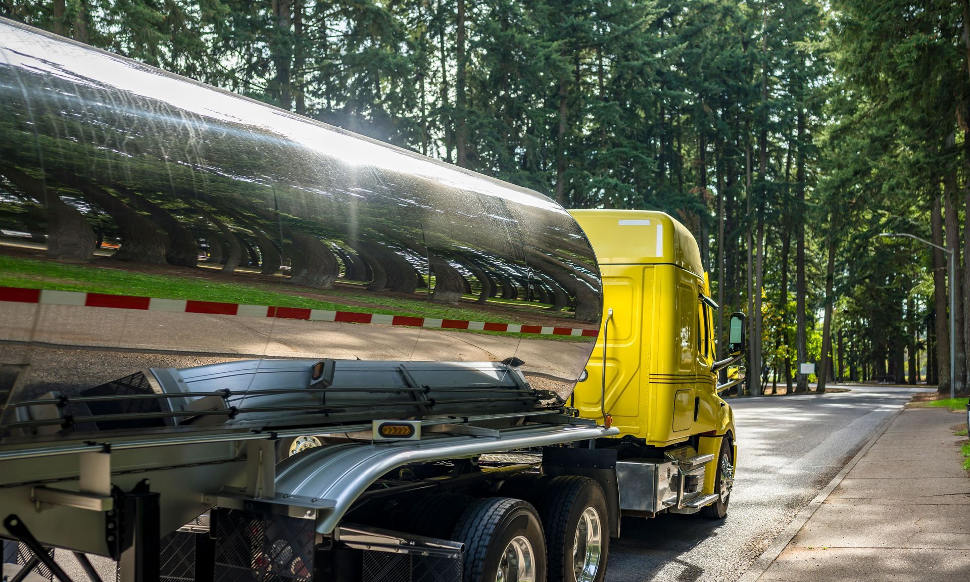 A yellow semi truck is driving down a road next to trees.