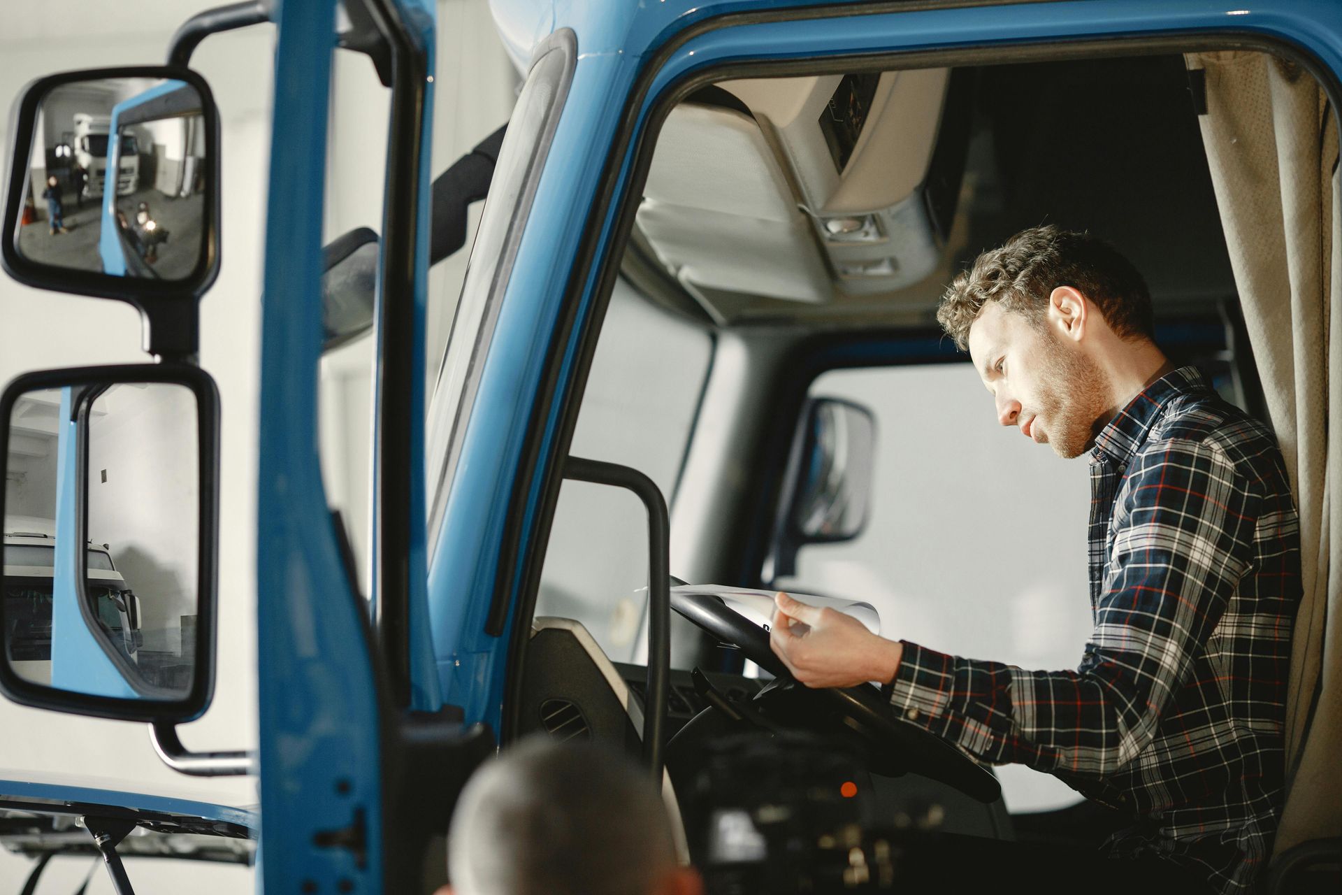A man is sitting in the driver 's seat of a truck looking at a tablet.