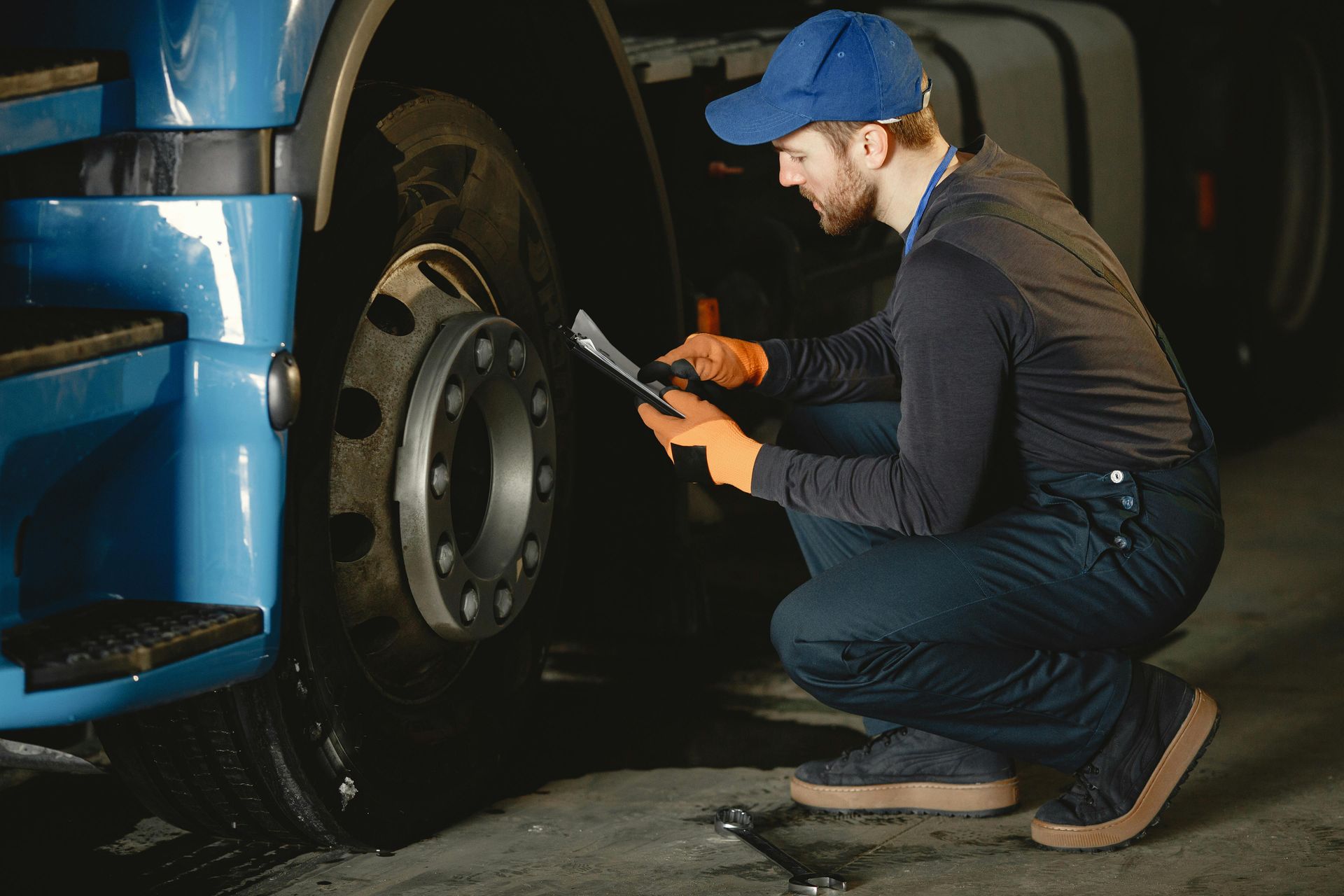 A man is kneeling down next to a truck and looking at a tablet.