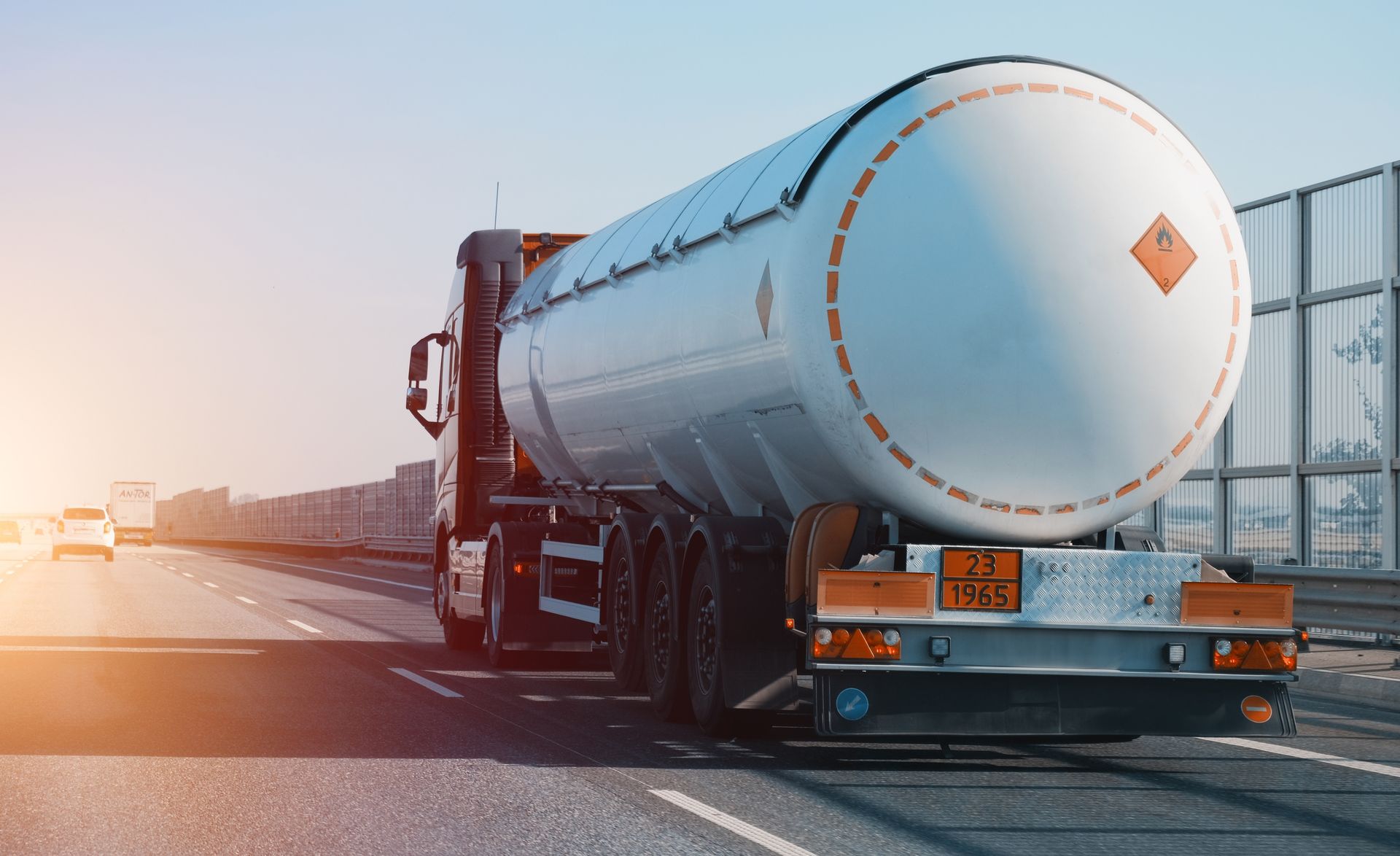 A tanker truck is driving down a highway with a large tank on the back.
